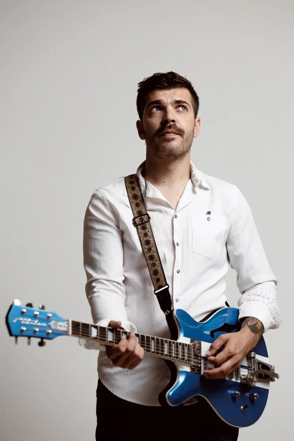 Matteo Leone in camicia bianca con la chitarra elettrica blu a tracolla, sguardo verso l'alto