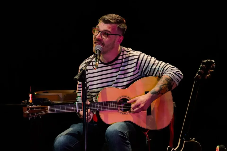 Matteo Leone in concerto, seduto con la chitarra acustica davanti al microfono